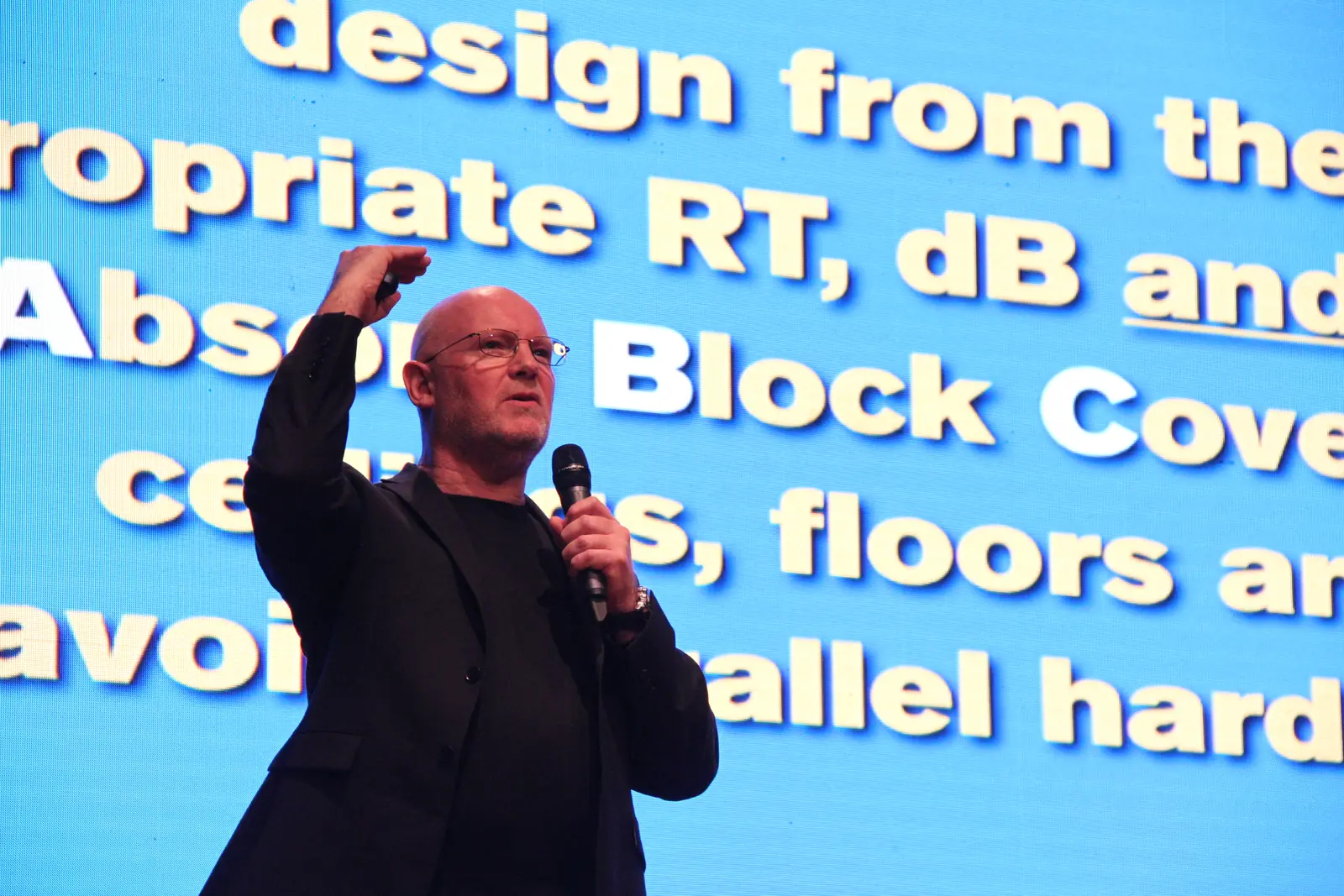 Julian Treasure speaking in front of a slide about acoustic design, Mumbai