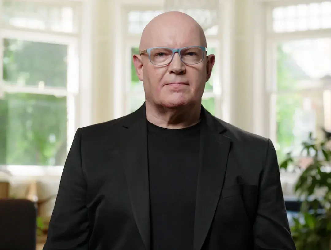 Julian Treasure in a black jacket, seated in a bright room with tall windows