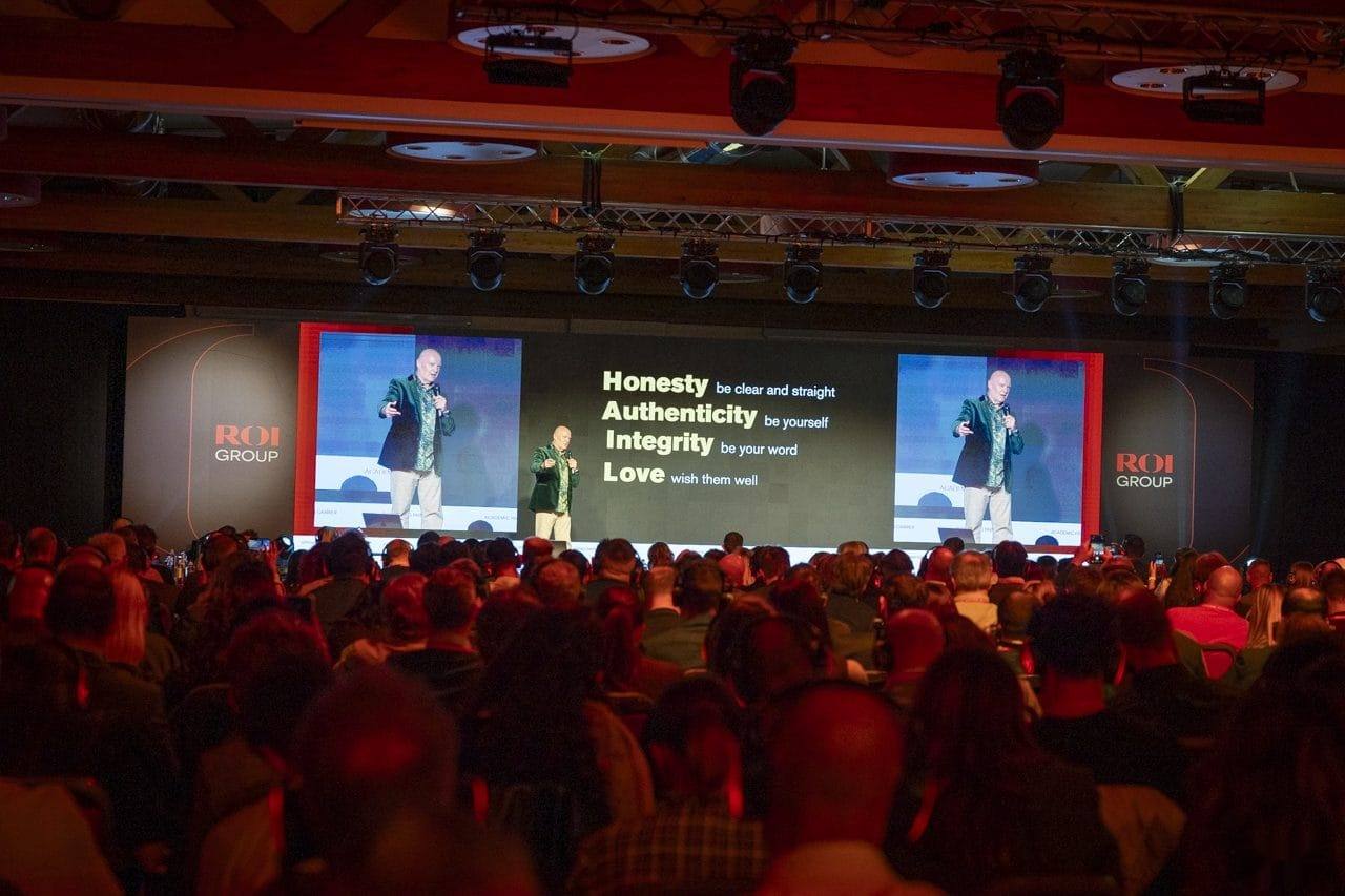 A packed conference hall, with Julian Treasure on the screens beside a slide reading Honesty, Authenticity, Integrity, Love