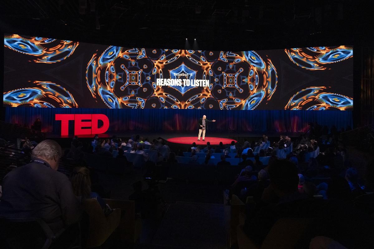 Julian Treasure on the red circle of the TED stage beneath a wide screen reading Reasons to Listen, the audience in the foreground